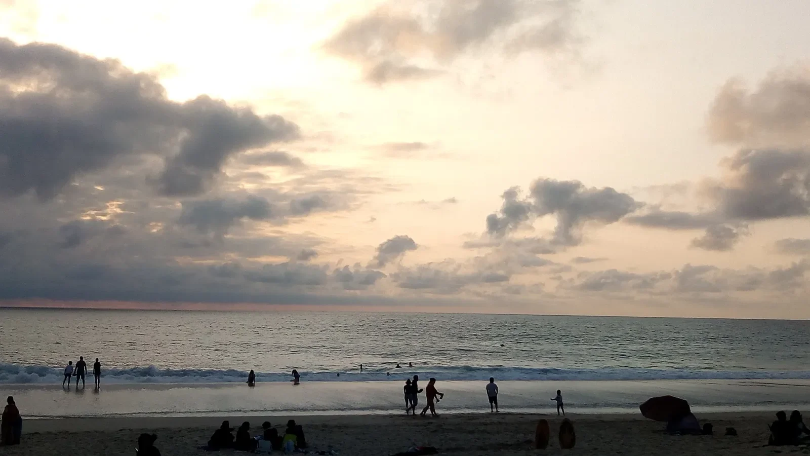 Un ciel de nuages aux teintes dorées au-dessus de la plage de Capbreton, avec les promeneurs en silhouette au bord de l'eau.