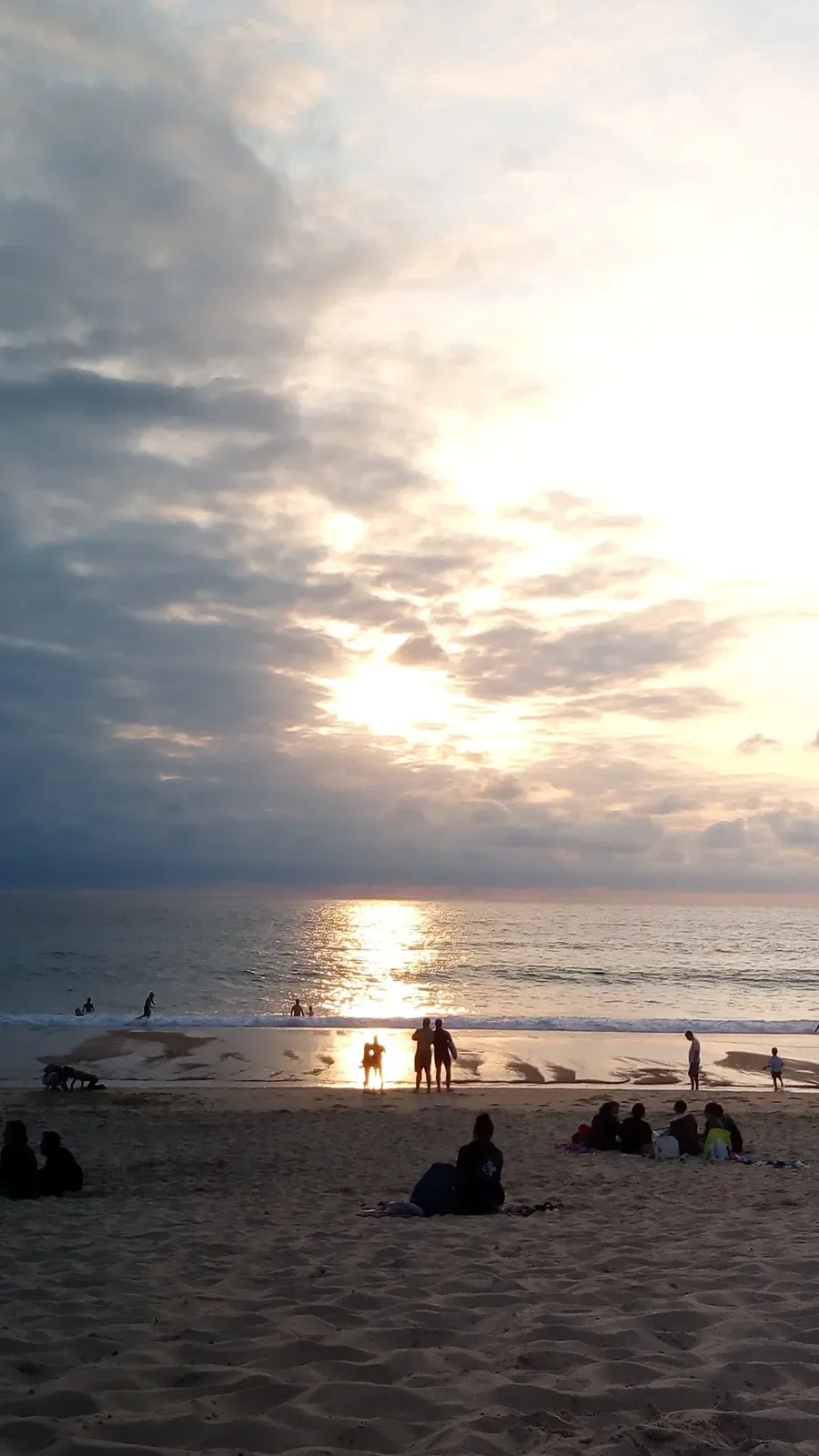 À Capbreton, des silhouettes face au soleil couchant, reflété sur le sable humide au bord de l'océan Atlantique.