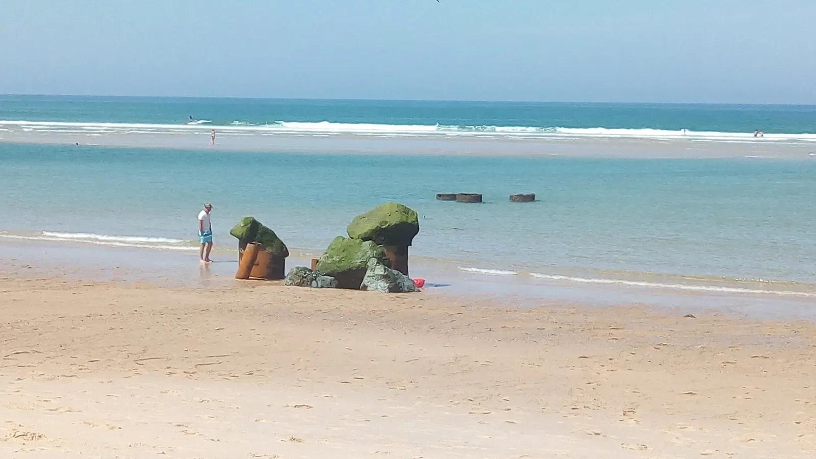 Un promeneur au bord de l'eau devant les blockhaus de la plage de Santocha, à Capbreton, sur le sable à marée basse.