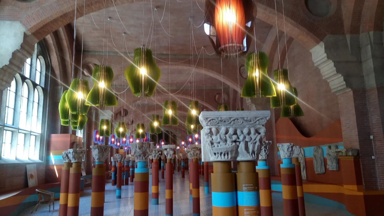 Dans le musée des Augustins à Toulouse, des chapiteaux sculptés sur des colonnes colorées, sous des suspensions lumineuses