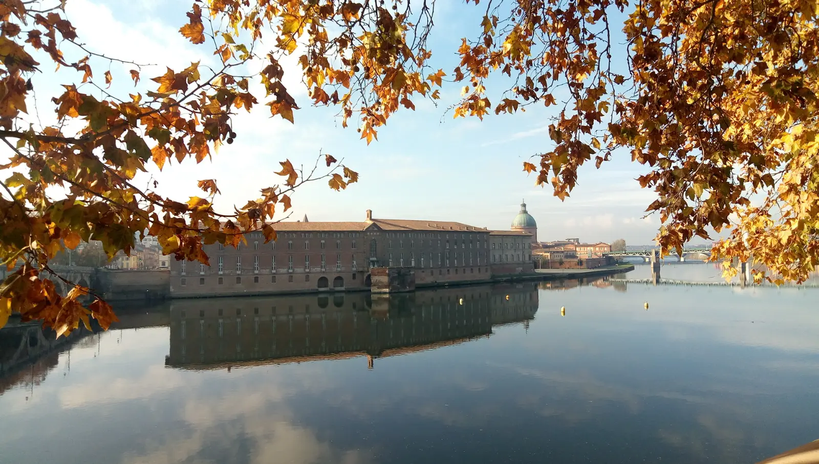 L’Hôtel-Dieu Saint-Jacques et le dôme de La Grave se reflètent dans la Garonne calme, sous les feuilles d’automne, à Toulouse.