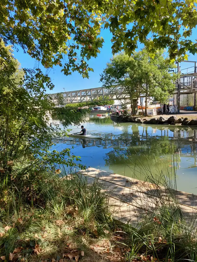 Un rameur glisse sur le Canal du Midi à Ramonville-Saint-Agne, devant la passerelle et un ponton ombragé