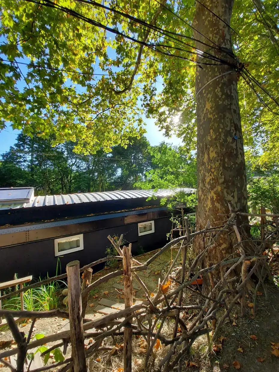 Une péniche noire au toit de tôle, à l'ombre d'un platane au tronc moucheté, au bord du Canal du Midi à Ramonville-Saint-Agne.