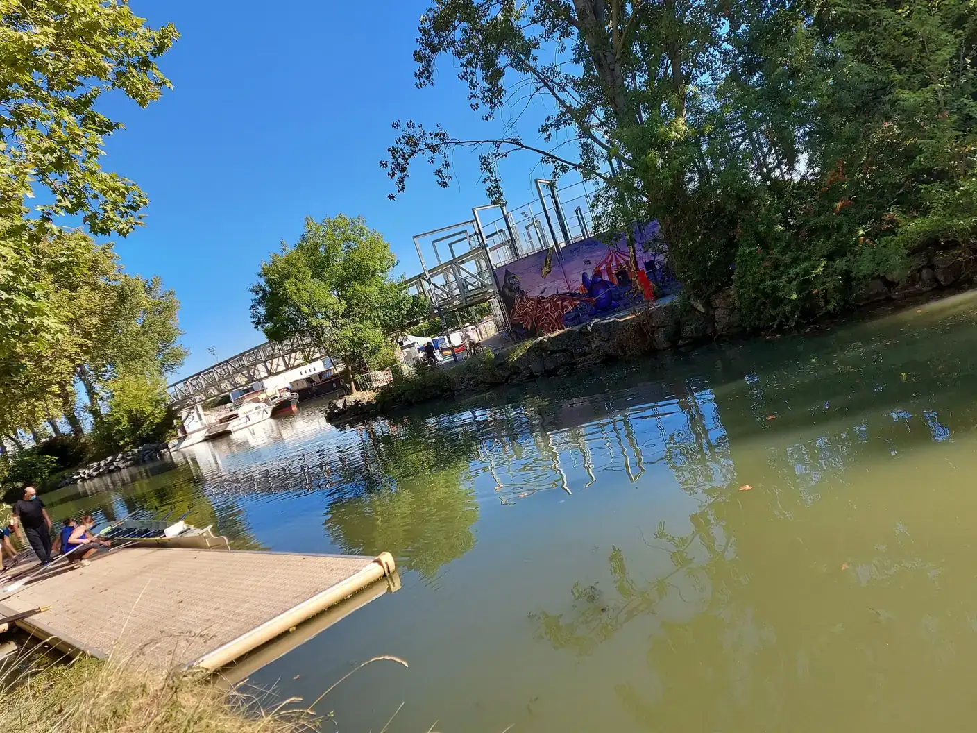 Un ponton et la passerelle du Canal du Midi à Ramonville-Saint-Agne, avec une fresque colorée sur le mur de la berge.
