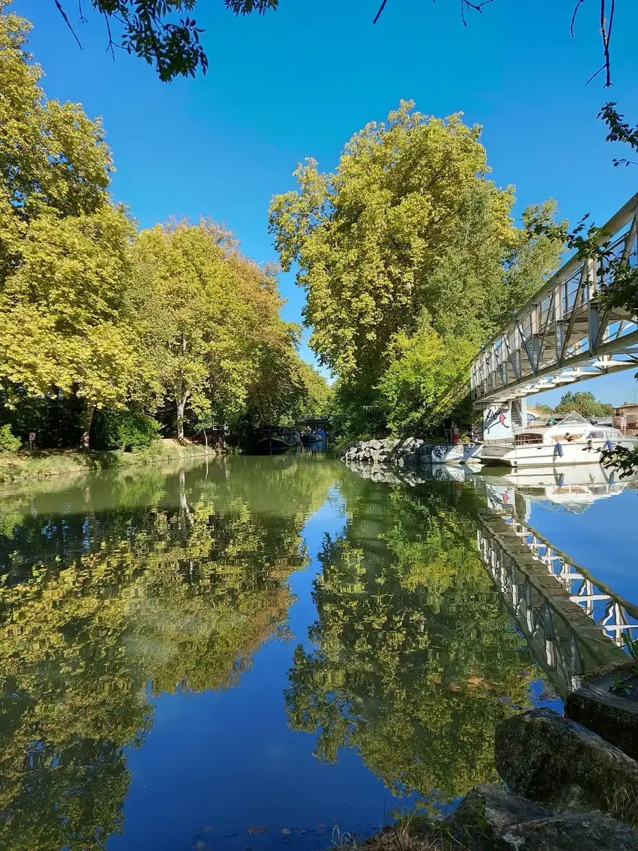 Reflets des platanes et d'une passerelle blanche dans les eaux calmes du Canal du Midi, à Ramonville-Saint-Agne.