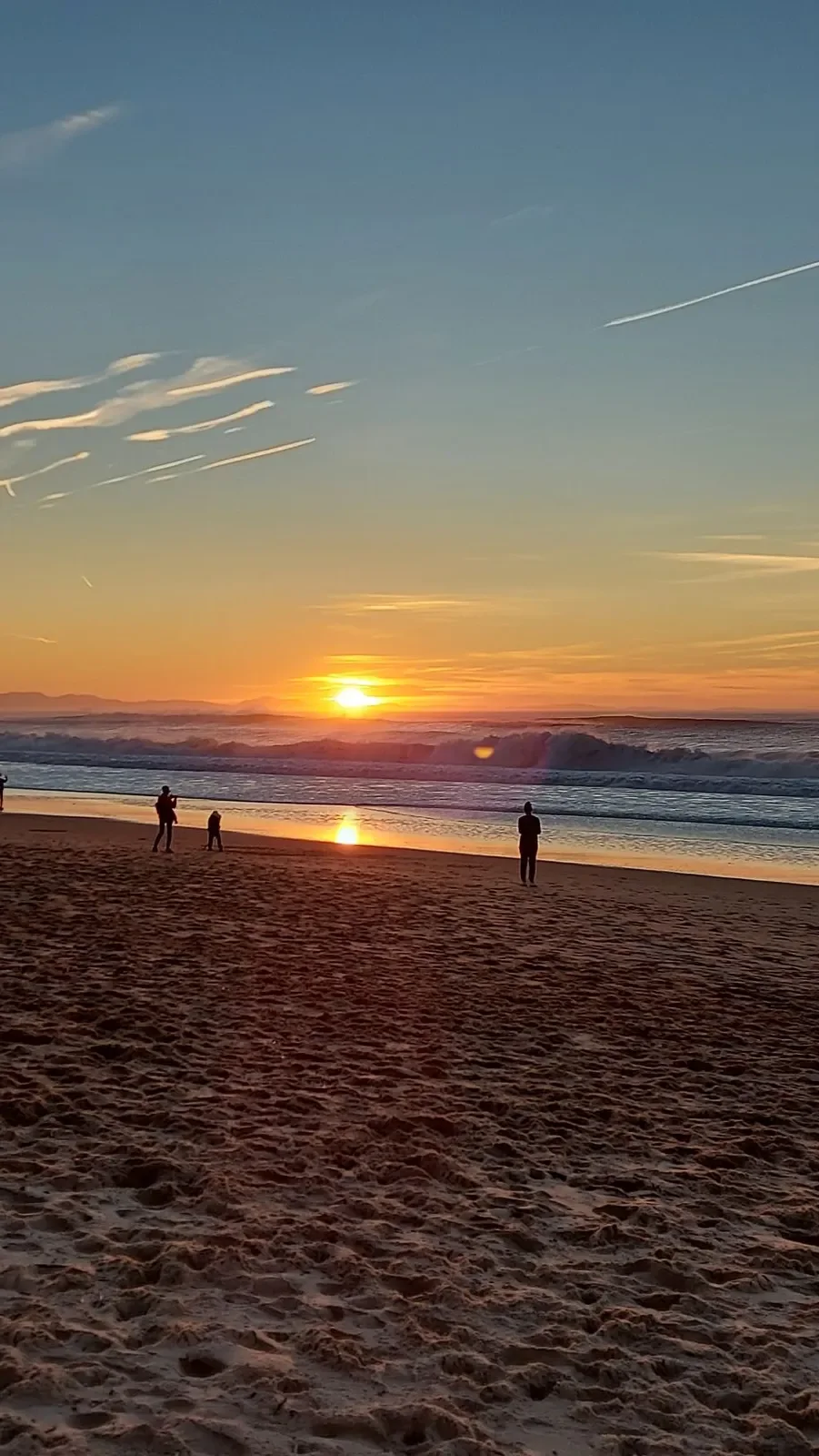 Le soleil se couche derrière les vagues à Capbreton : des silhouettes se détachent sur le sable, sous un ciel orange et bleu, le 31 décembre 2021.