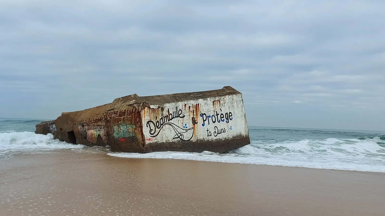 Un blockhaus échoué sur la plage de Santocha, à Capbreton, porte l'inscription « Déambule & protège ta dune… » au milieu des vagues.