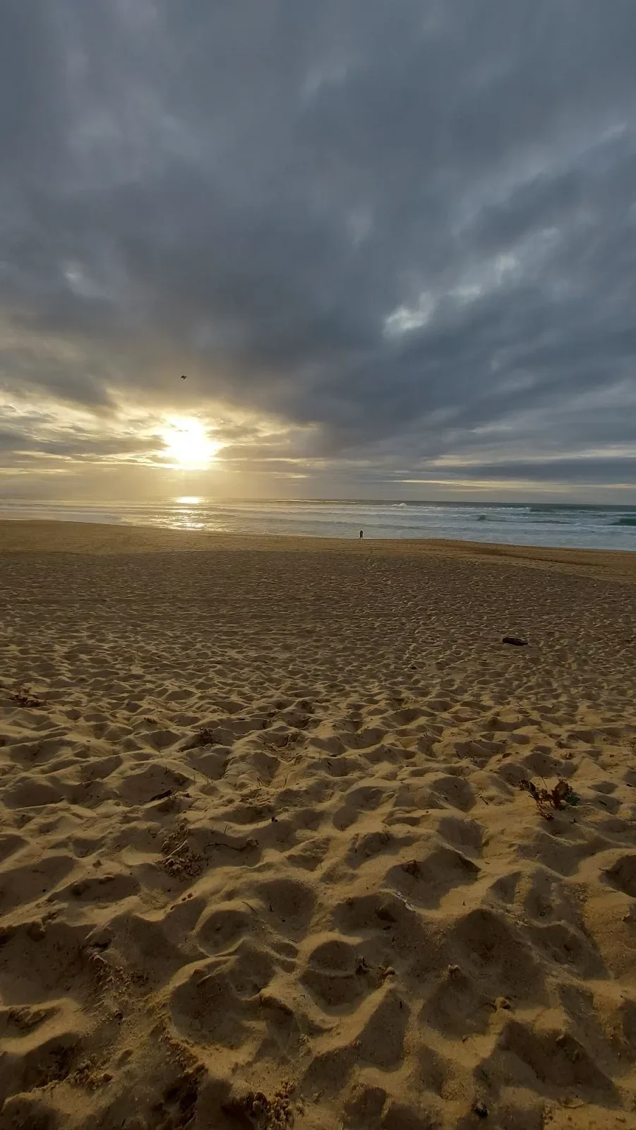 Le soleil couchant filtre entre les nuages sur la plage de Capbreton, au-dessus d'un sable creusé de traces de pas.