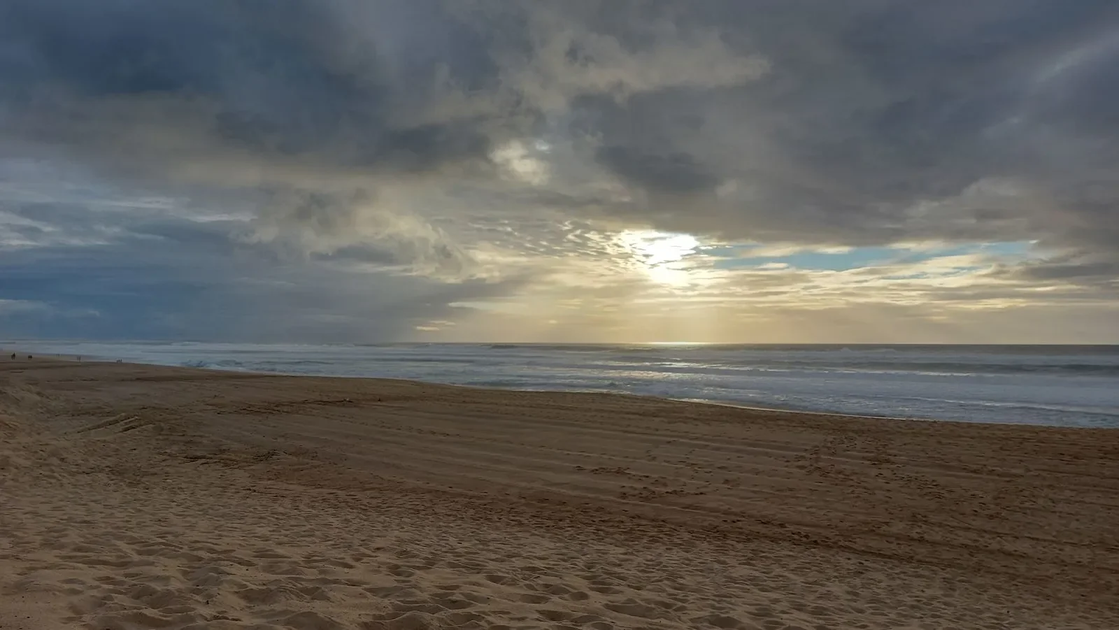 Le soleil perce les nuages au-dessus de la plage de Capbreton, sur le sable et les vagues, en novembre.
