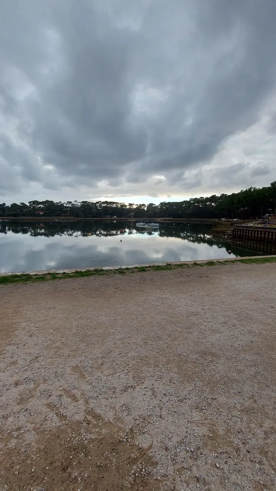 Le lac marin d’Hossegor reflète les nuages et les pins, vu depuis un chemin de gravier sur la berge.