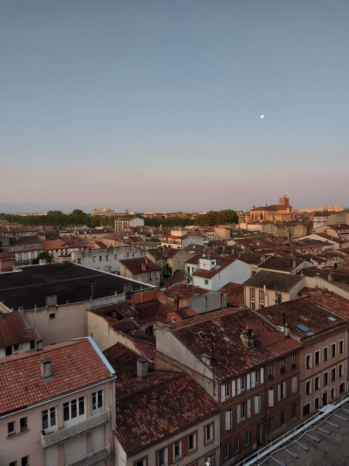 La lune qui se lève au-dessus des toits, quand la lumière devient rose.