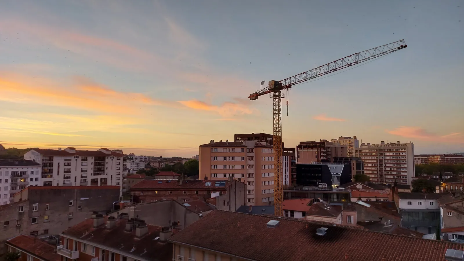 Grue de chantier jaune pour le métro et immeubles de Toulouse devant un lever de soleil orange