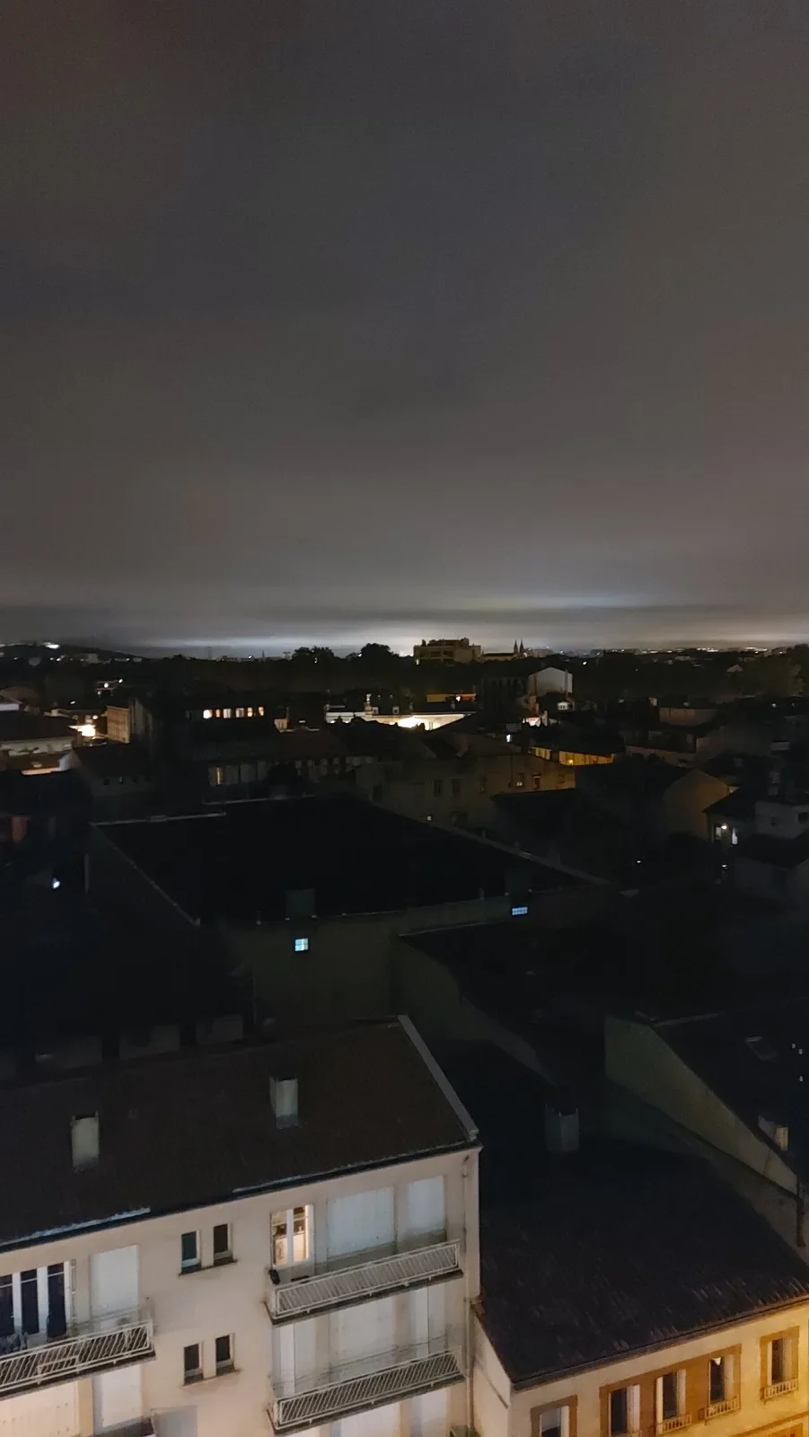Toits de Toulouse la nuit, sous des nuages éclairés par la lumière de la ville