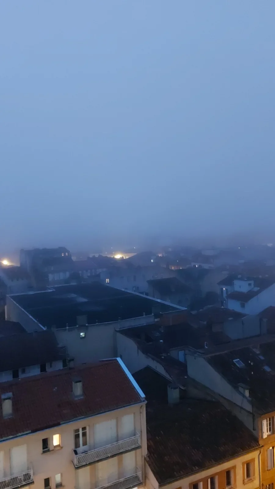 Un matin de brouillard bleu : la ville disparaît et les lumières restent.