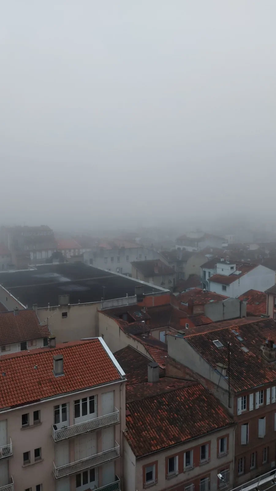 Brouillard épais, il ne reste que les toits au premier plan.