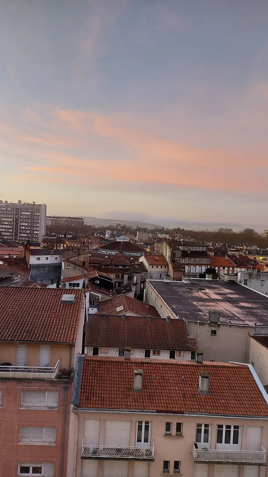 Un ciel rose et orange, et les Pyrénées au loin dans la brume.
