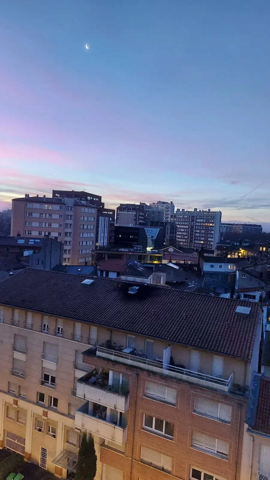 Fin croissant de lune dans un ciel bleu et rose au-dessus des immeubles de Toulouse