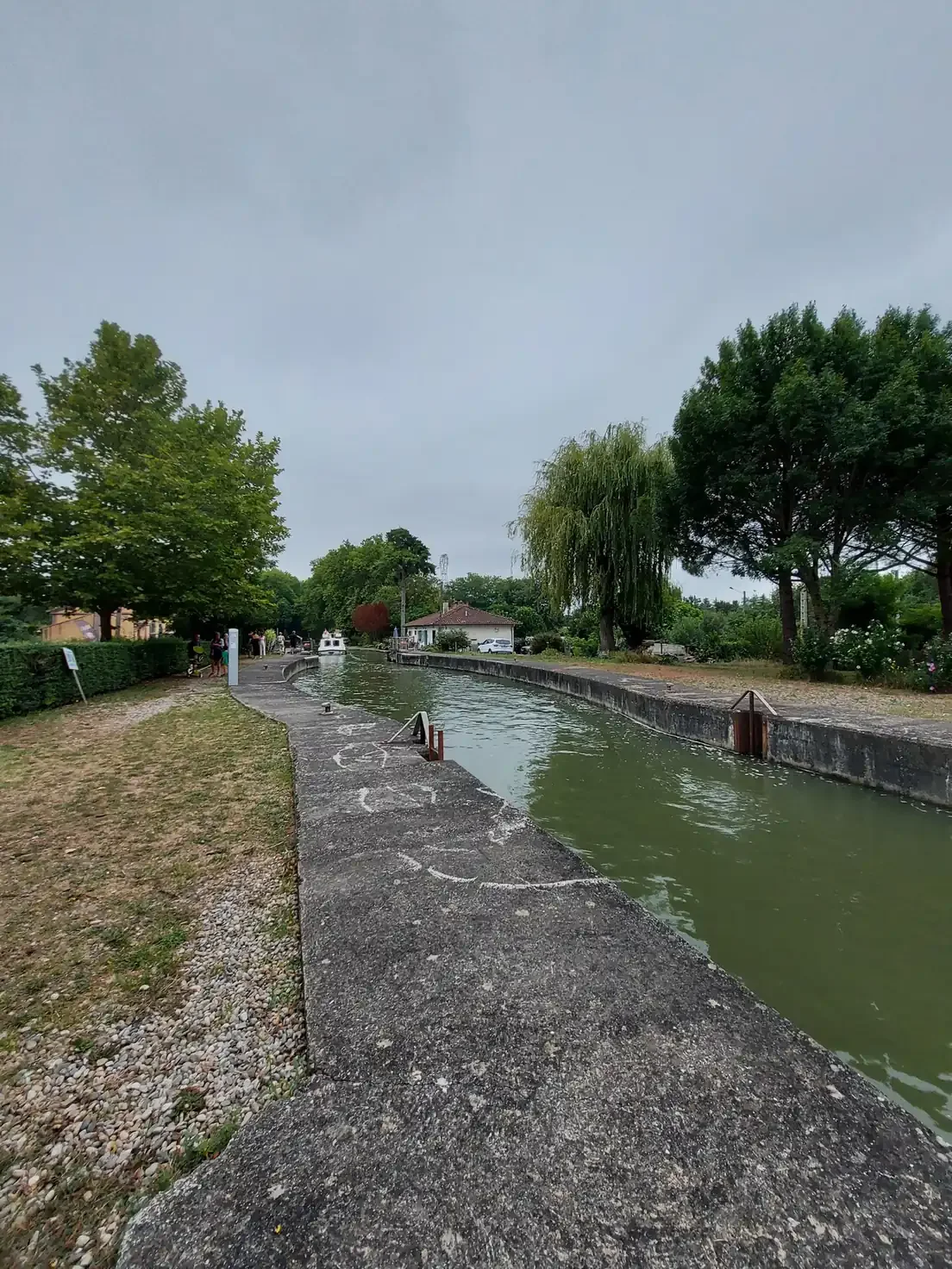 Sas d'une écluse du canal du Midi vu depuis le bord, avec une péniche au loin et la maison éclusière