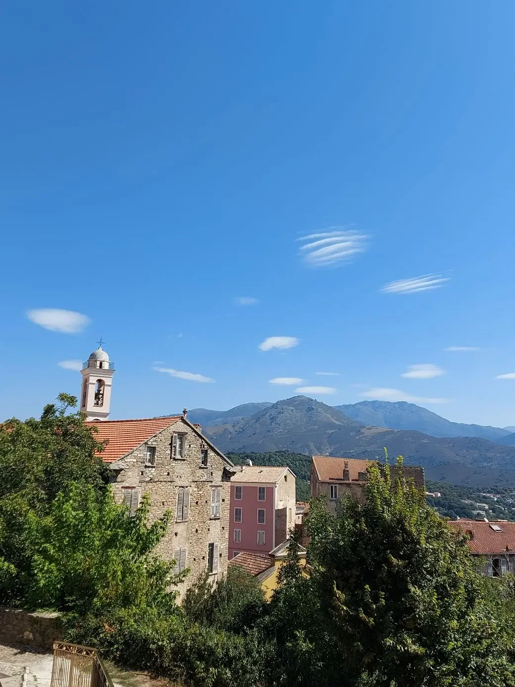 Clocher rose et maisons de pierre de Corte devant les montagnes corses