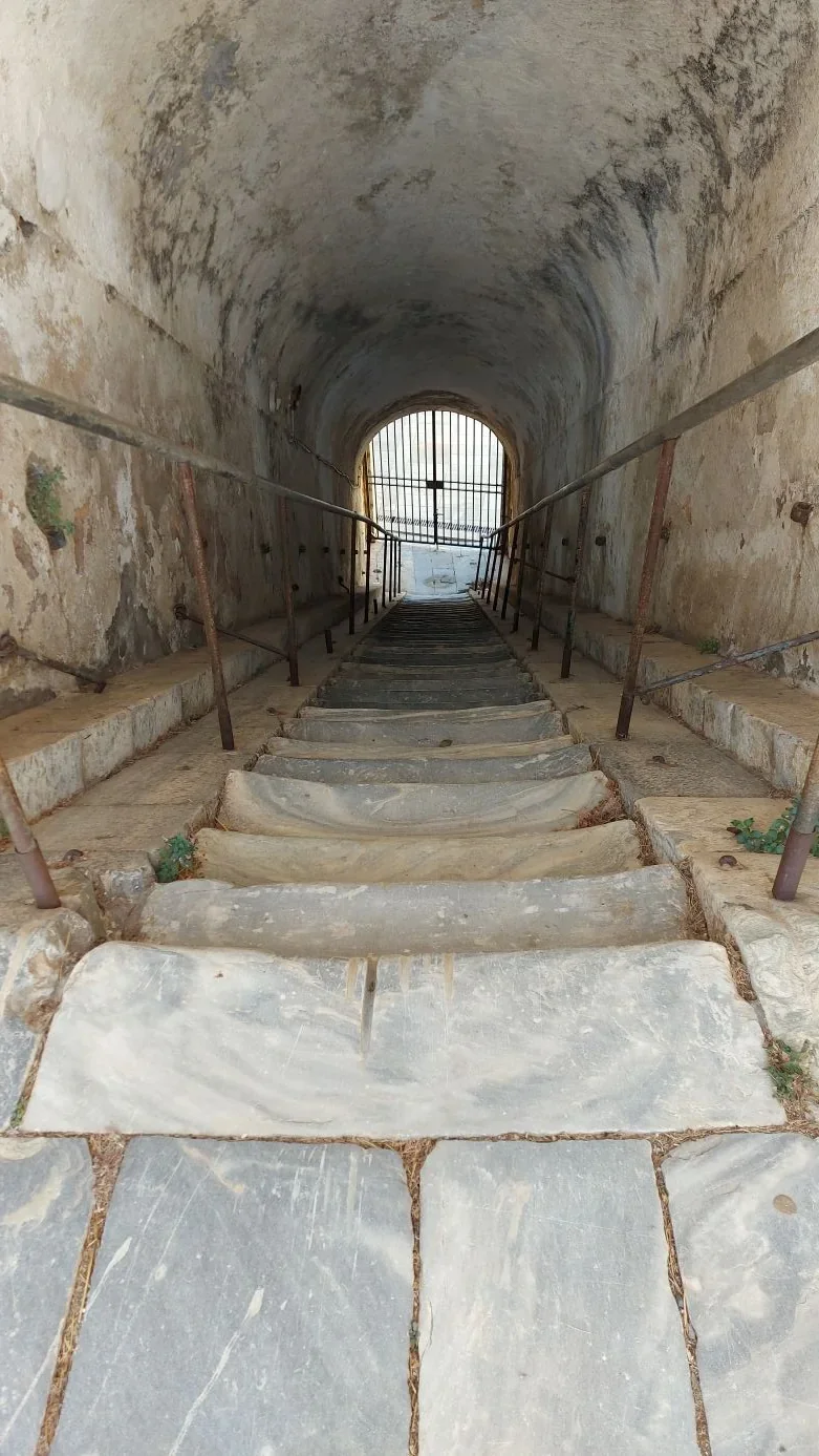 Escalier de pierre dans un passage voûté de la citadelle de Corte, grille ouverte sur la lumière