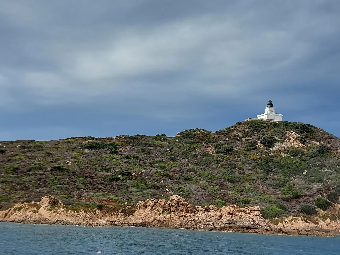 Phare des Iles sanguinaires au sommet d'une colline de maquis, vu depuis la mer, ciel d'orage