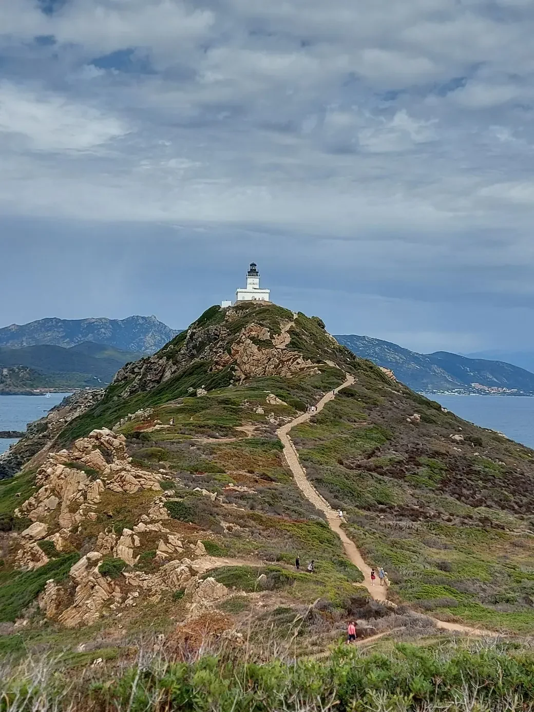 Sentier en lacets montant vers le phare blanc des îles Sanguinaires, entre rochers et maquis.